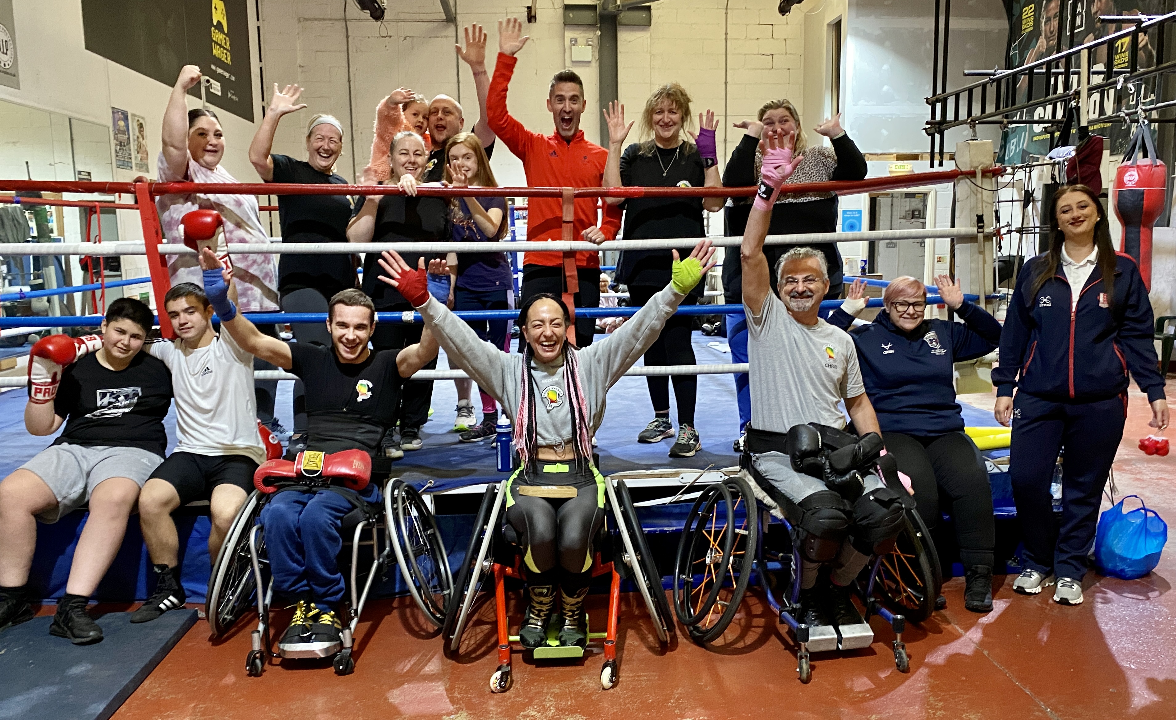 All members of Kronik Warrior adaptive boxing club, stood and sat at the ring side with arms in the air celebrating their Club of the Month award hand over.