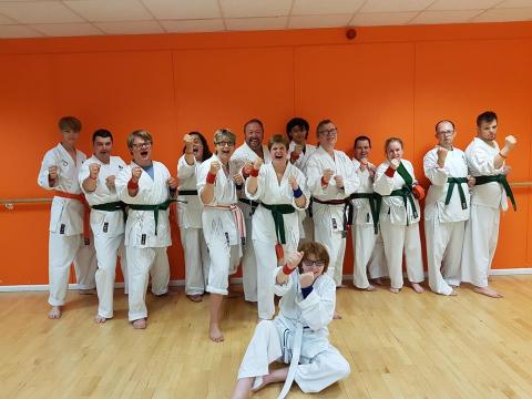 Group of disabled and non-disabled people laughing and wearing karate suits and their new green belts. One person is stting on the floor