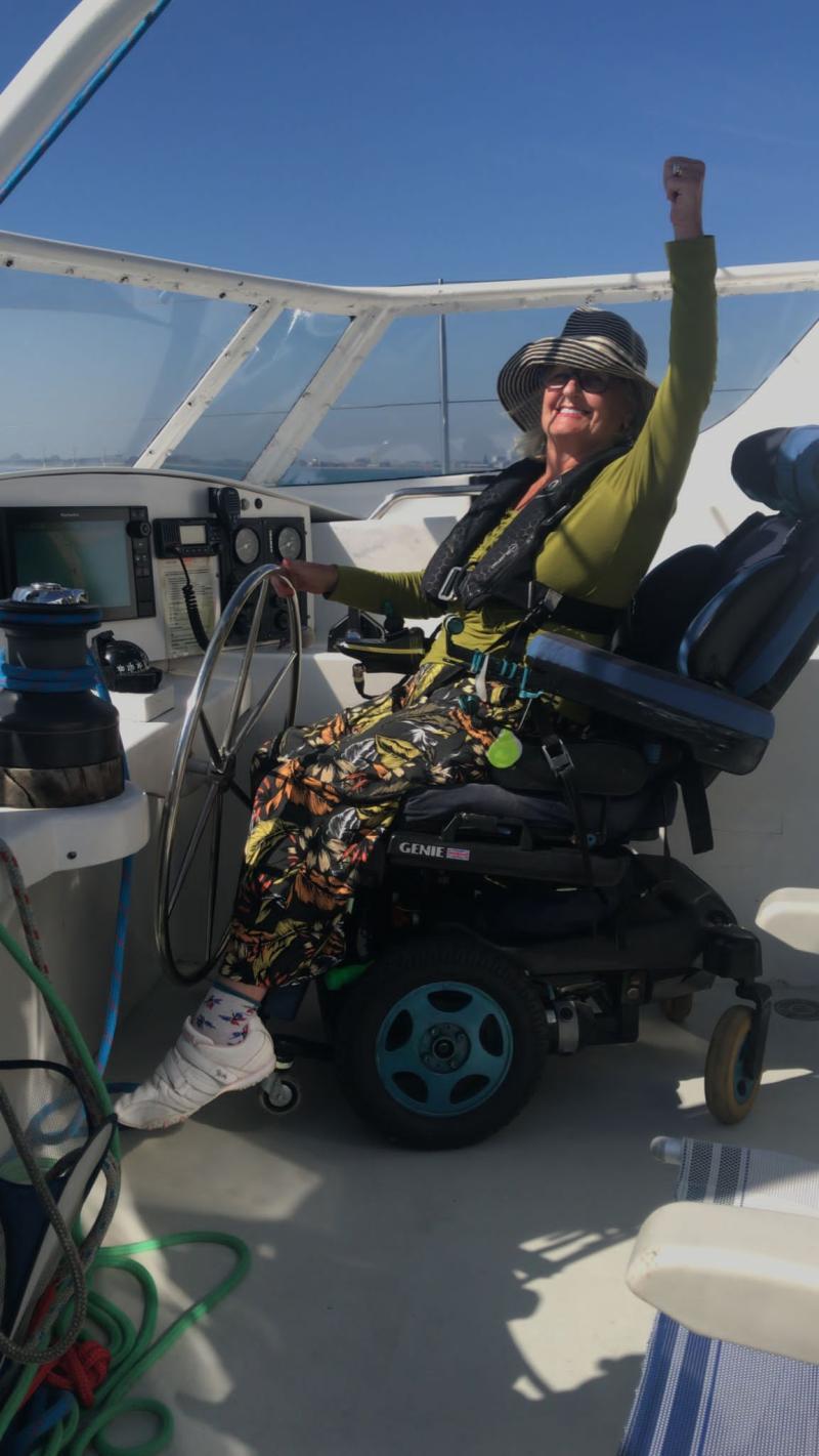 A very happy woman in an electric wheelchair raising her hand in the air and smiling 